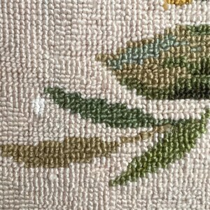 May include: Close-up of a beige rug with a green and brown floral design. The rug is made of a soft, textured material.
