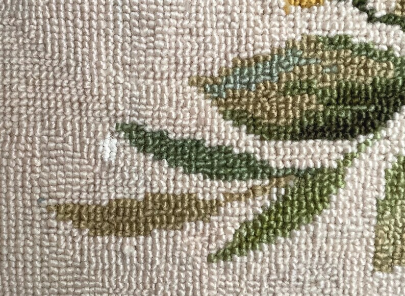 May include: Close-up of a beige rug with a green and brown floral design. The rug is made of a soft, textured material.