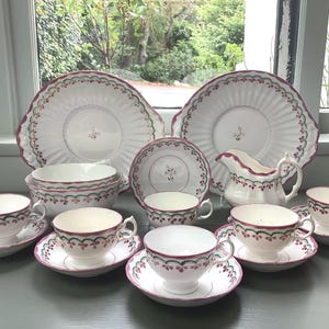 Puede incluir: Un juego de té vintage con un patrón floral rosa y verde. El juego incluye una tetera, una jarra de crema, un azucarero y cuatro tazas de té y platillos.