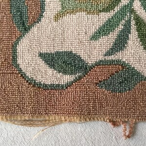May include: Close-up of the edge of a brown, cream, and green rug with a floral pattern. The rug is made of woven yarn and has a frayed edge.