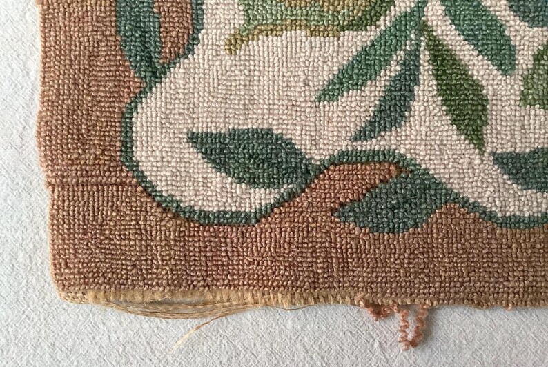 May include: Close-up of the edge of a brown, cream, and green rug with a floral pattern. The rug is made of woven yarn and has a frayed edge.