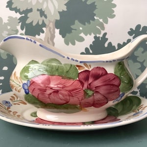 Puede incluir: Una salsera de cerámica blanca con un diseño floral. La salsera tiene un patrón floral rosa, rojo y verde con acentos azules. La salsera está sentada sobre un platillo a juego.