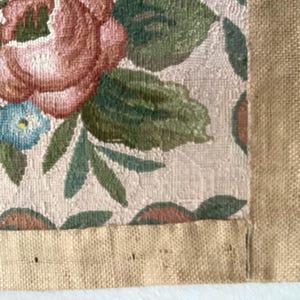 May include: A close-up of a beige fabric with a floral pattern. The fabric has a brown burlap border.