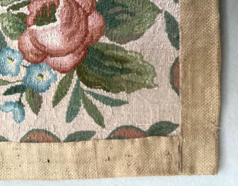 May include: A close-up of a beige fabric with a floral pattern. The fabric has a brown burlap border.