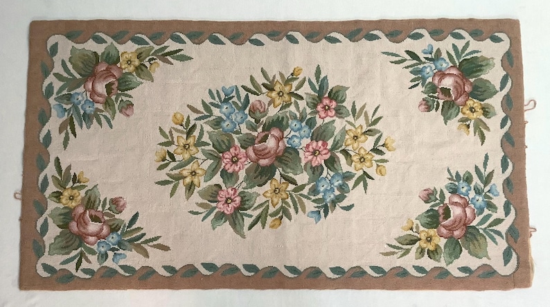 May include: A beige rug with a brown border and a floral design. The rug features pink, yellow, and blue flowers with green leaves.