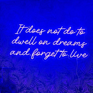 May include: Neon sign with the quote "It does not do to dwell on dreams and forget to live" against a purple and black tropical leaf pattern background.