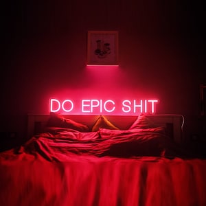 Pu&ograve; includere: Un letto rosso con cuscini bianchi e un cartello al neon che recita "DO EPIC SHIT" sopra la testiera.