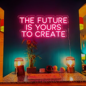 Könnte beinhalten: Ein pinkfarbenes Neon-Schild mit dem Text "The future is yours to create." Das Schild hängt an einer türkisfarbenen Wand mit einer Topfpflanze und zwei Lampen auf einem Tisch davor.