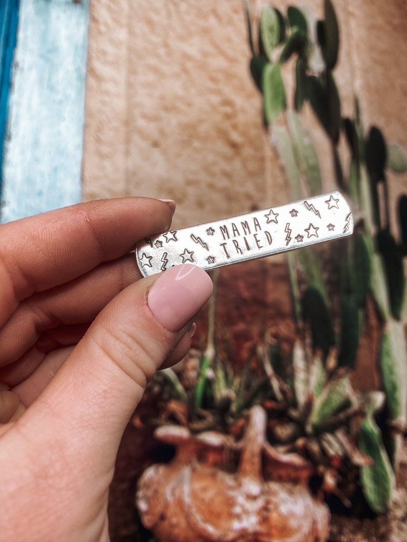 May include: Silver metal bar with the text "Mama Tried" engraved on it. The bar is decorated with small stars and lightning bolts.