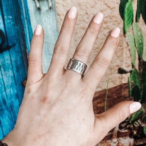 May include: A silver ring with the words "Mama'z Tried" engraved on it. The ring is worn on the middle finger of a hand with light pink nail polish.