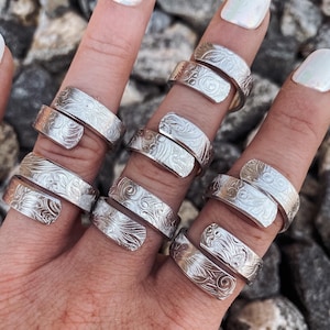 May include: A set of six silver rings with a swirling, floral design. The rings are adjustable and can be worn on any finger.
