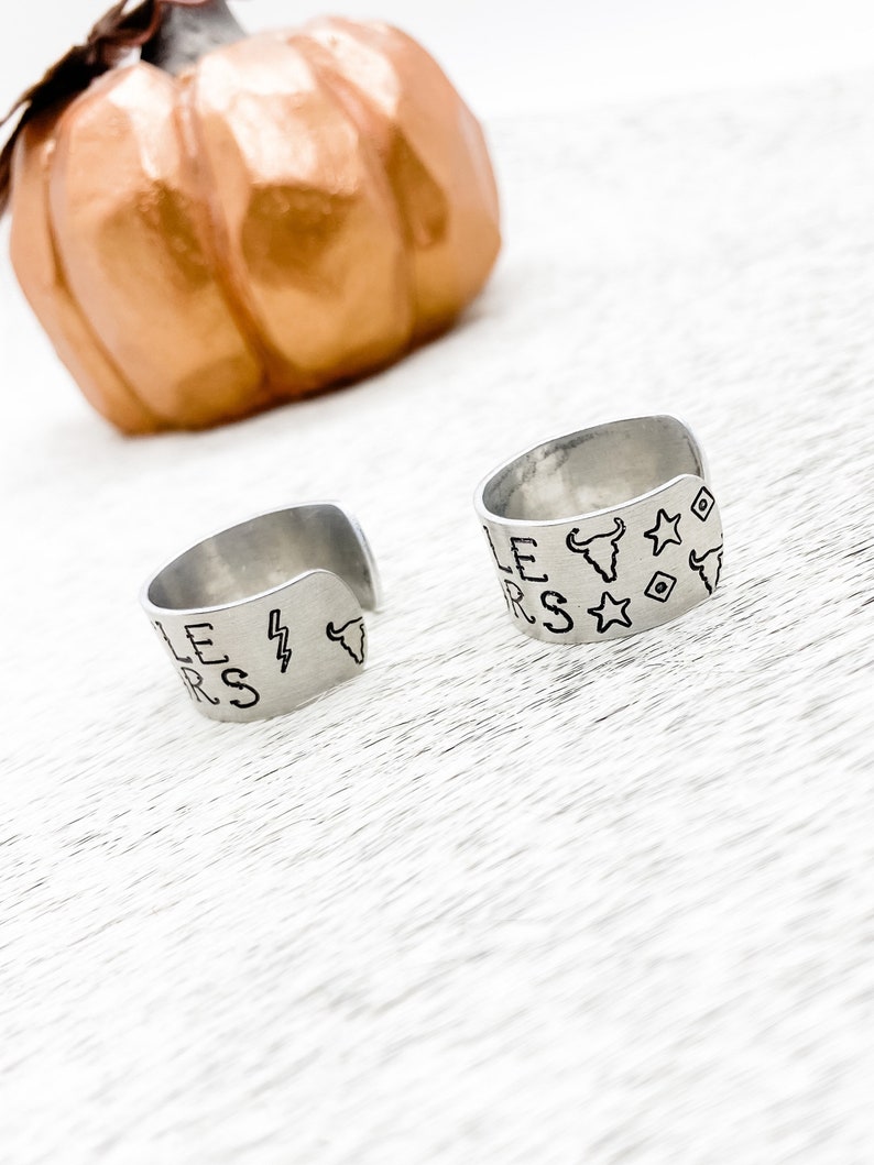 May include: Two silver rings with engraved designs. One ring has the words "Little" and "Stars" engraved on it, along with a lightning bolt and a bull's head. The other ring has the words "Little" and "Stars" engraved on it, along with a bull's head and stars.