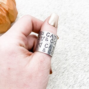 May include: Two silver rings with the text "Cattle & Co" engraved on them. The rings are worn on a person's thumb.