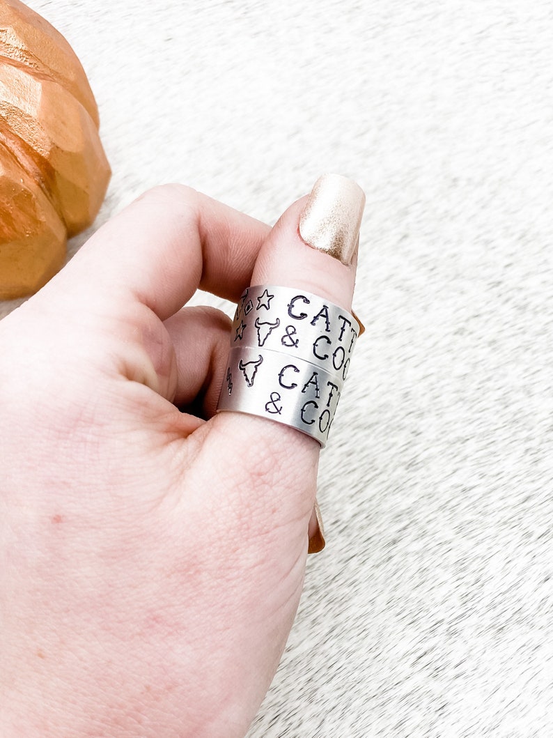 May include: Two silver rings with the text "Cattle & Co" engraved on them. The rings are worn on a person's thumb.