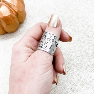May include: Two silver rings with the words "Little Stars" and "Little Riders" engraved on them. The rings are worn on a person's thumb.