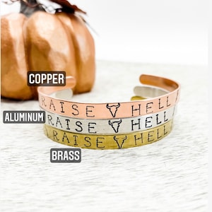 May include: Three stacked bracelets with the words "Raise Hell" and a bull's head symbol. The bracelets are made of copper, aluminum, and brass.