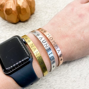 Puede incluir: Tres pulseras de oro, plata y oro rosa con un dise&ntilde;o de cactus y coraz&oacute;n. Las pulseras est&aacute;n grabadas con las palabras "MOMMA", "AUNTIE" y "NANA".