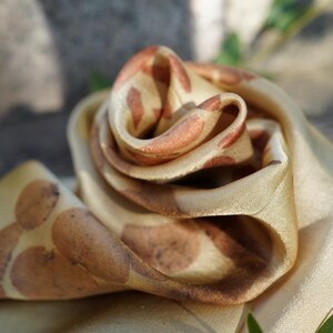 Pu&ograve; includere: Una sciarpa in tessuto liscio color oro con un motivo ripetitivo di stampe botaniche arrotondate color ruggine. Il materiale &egrave; piegato in una forma a rosa a strati, che mette in risalto la lucentezza morbida e le macchie organiche color marrone terra.