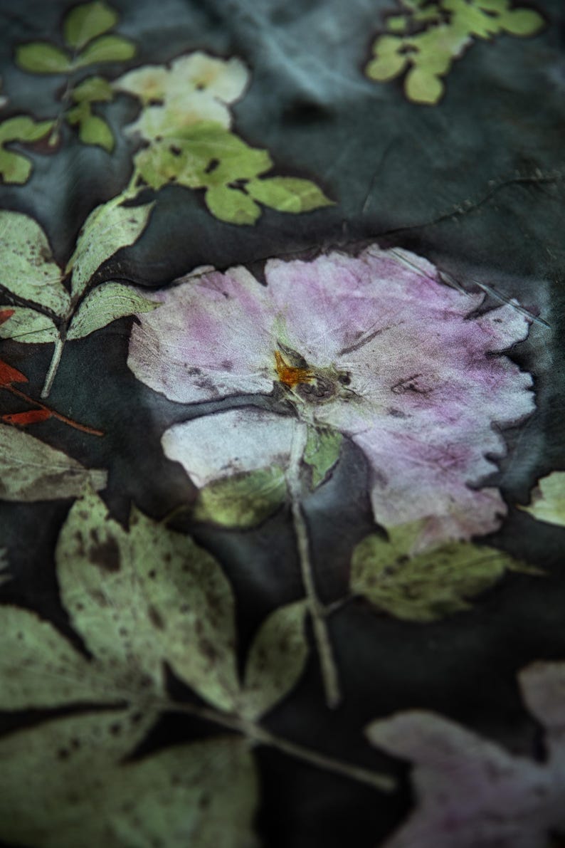 May include: A dark charcoal fabric featuring a botanical print with a large, pale pink flower at the center. The design includes detailed green leaves and stems scattered across the surface, creating a natural, pressed-flower appearance.