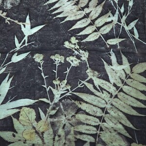 May include: A dark charcoal fabric featuring a botanical print with light cream-colored silhouettes of various ferns, leaves, and small clusters of wildflowers. The pattern displays intricate vein details on the foliage against a textured background.