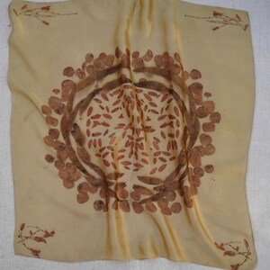 Pu&ograve; includere: Un foulard quadrato in seta color giallo pallido con una stampa botanica circolare centrale composta da motivi di foglie e baccelli marroni. I quattro angoli del foulard sono decorati con piccoli e delicati rametti con motivi vegetali marroni.