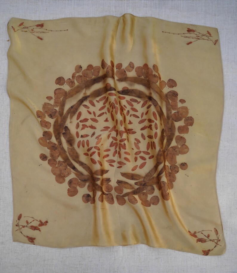 Pu&ograve; includere: Un foulard quadrato in seta color giallo pallido con una stampa botanica circolare centrale composta da motivi di foglie e baccelli marroni. I quattro angoli del foulard sono decorati con piccoli e delicati rametti con motivi vegetali marroni.