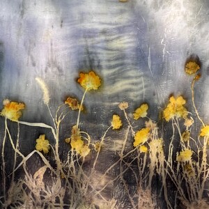 May include: A rectangular piece of fabric featuring a botanical print with pressed yellow flowers and thin stems against a textured, mottled background of grey, blue, and white tones. A small, circular, light-colored element is visible at the top.