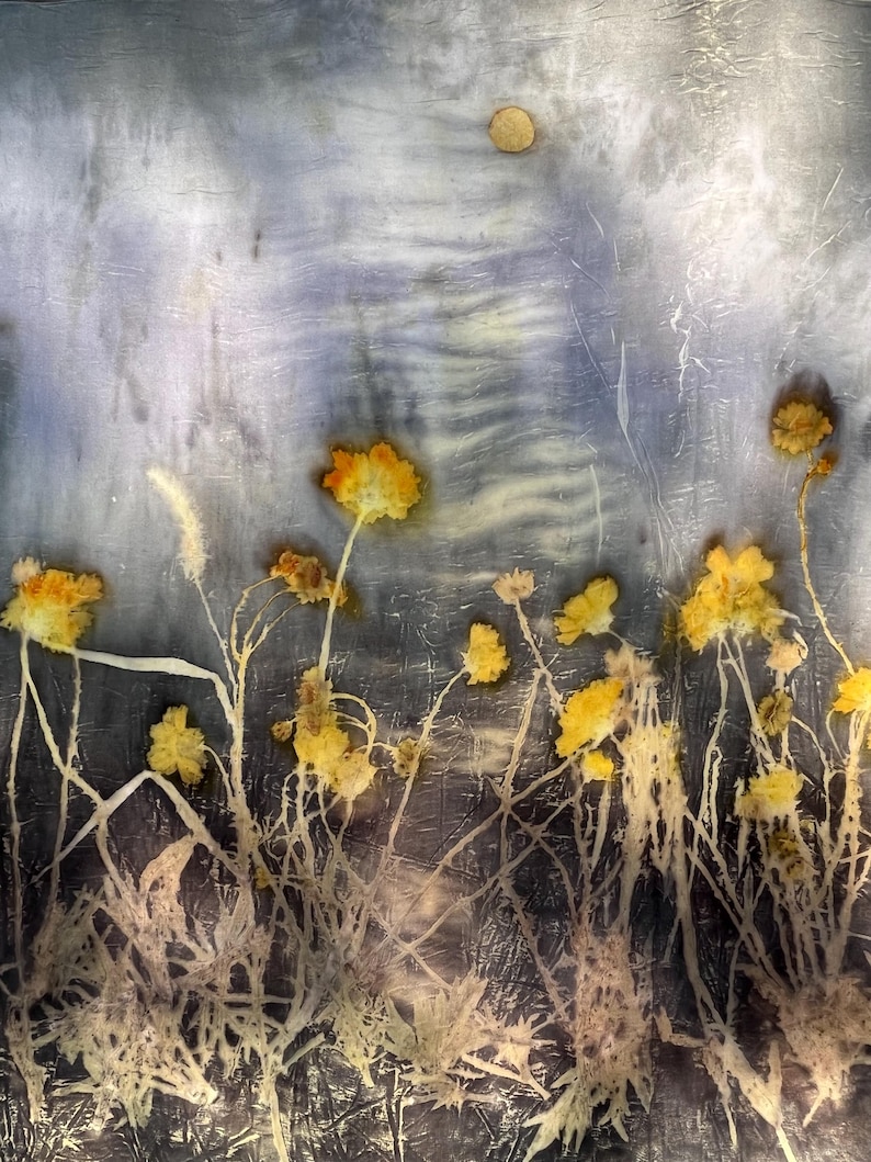 May include: A rectangular piece of fabric featuring a botanical print with pressed yellow flowers and thin stems against a textured, mottled background of grey, blue, and white tones. A small, circular, light-colored element is visible at the top.