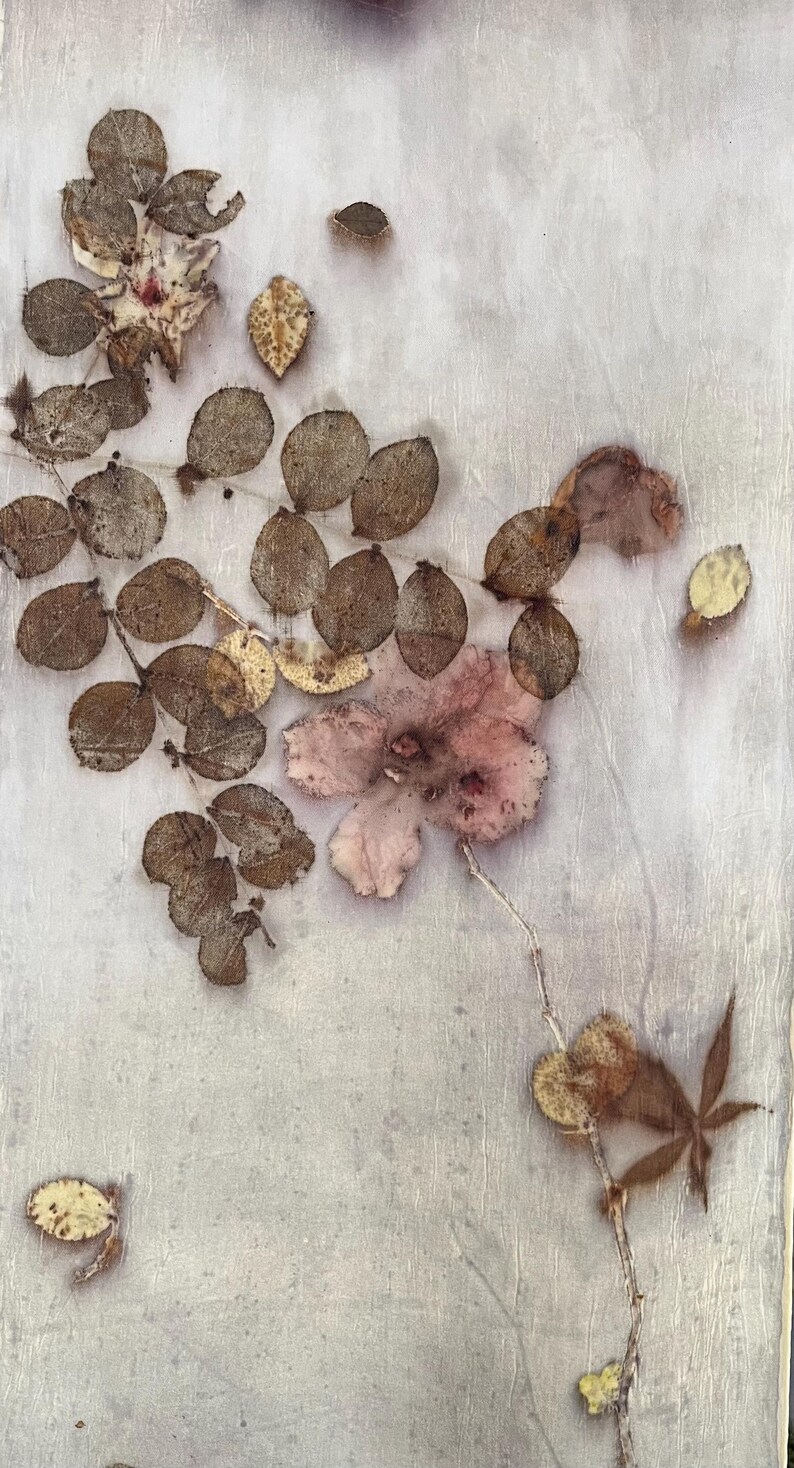May include: A light-coloured textile featuring a botanical print of pressed brown leaves and a single pale pink flower. The design includes a cluster of small, rounded foliage arranged along a stem, with scattered individual leaves across the surface.