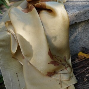Pu&ograve; includere: Un foulard rettangolare in seta di una delicata tonalit&agrave; giallo oro, caratterizzato da delicate impronte botaniche nei toni del ruggine e del marrone. Il tessuto ha una finitura liscia e lucente con bordi cuciti visibili e motivi vegetali.