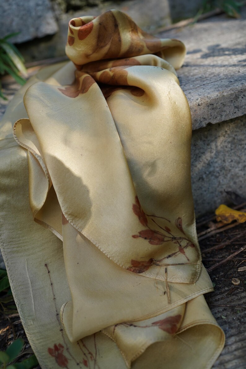 Pu&ograve; includere: Un foulard rettangolare in seta di una delicata tonalit&agrave; giallo oro, caratterizzato da delicate impronte botaniche nei toni del ruggine e del marrone. Il tessuto ha una finitura liscia e lucente con bordi cuciti visibili e motivi vegetali.