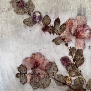 May include: A light-coloured textile featuring botanical prints of pink flowers and dark brown leaves. The fabric displays a subtle, textured surface with organic, pressed plant patterns scattered across the material in a natural, asymmetrical arrangement.