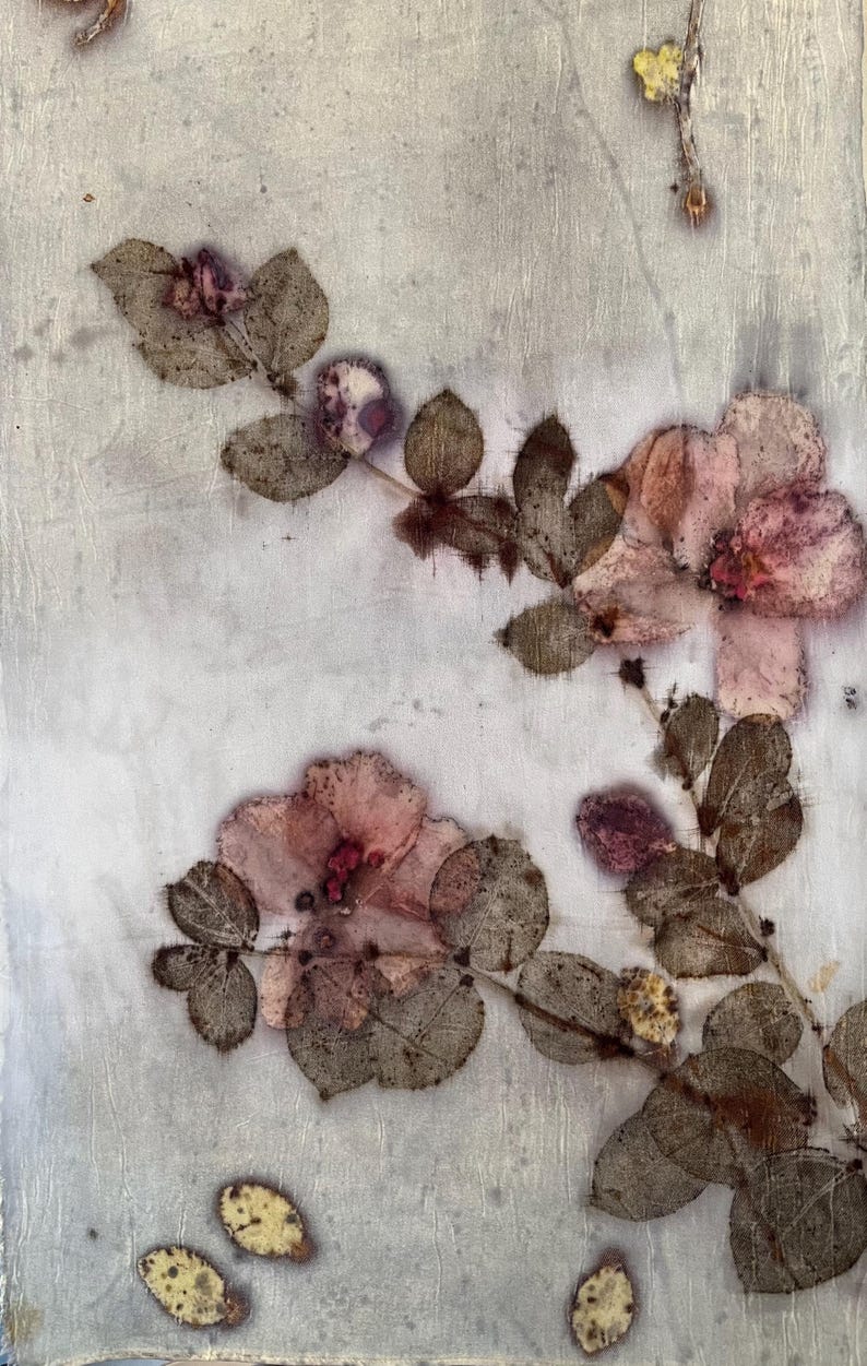 May include: A light-coloured textile featuring botanical prints of pink flowers and dark brown leaves. The fabric displays a subtle, textured surface with organic, pressed plant patterns scattered across the material in a natural, asymmetrical arrangement.