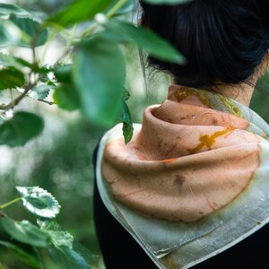 May include: A square scarf featuring a soft peach and cream color palette with organic, botanical-inspired leaf imprints in shades of rust and brown. The fabric has a delicate, semi-sheer texture and is folded around the neck in a layered style.