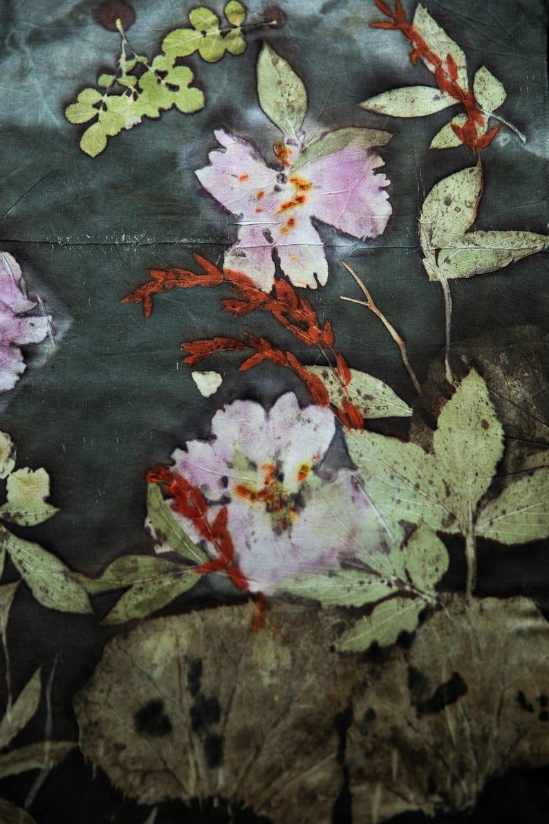 May include: A dark gray fabric featuring a botanical print with pressed light pink flowers, vibrant green leaves, and slender reddish-brown stems. The natural plant patterns are distributed across the surface, creating a detailed floral composition.