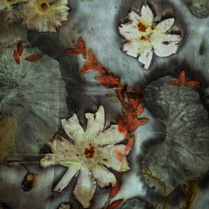 May include: A textile featuring a botanical print with pressed white flowers, large grey-green leaves, and a central orange-red branch. The fabric has a crinkled texture with dark, moody shadows and organic, earth-toned plant imprints throughout.