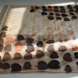May include: A square textile piece featuring a grid-like arrangement of dark brown and muted orange circular leaf-like imprints on a cream-coloured background. The fabric displays a subtle, semi-sheer texture with organic botanical patterns throughout.