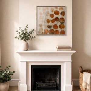 May include: A square framed wall art piece featuring a repeating pattern of circular, pressed orange and brown leaves arranged on a light, neutral background. The artwork is enclosed in a thin, light-coloured wooden frame with a visible grain texture.