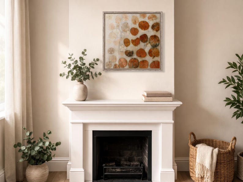 May include: A square framed wall art piece featuring a repeating pattern of circular, pressed orange and brown leaves arranged on a light, neutral background. The artwork is enclosed in a thin, light-coloured wooden frame with a visible grain texture.