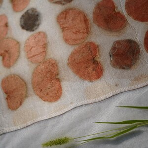 K&ouml;nnte beinhalten: Ein rechteckiges, cremewei&szlig;es Textil mit einem sich wiederholenden Muster aus gepressten, herzf&ouml;rmigen Bl&auml;ttern in Terrakotta-, Pfirsich- und Dunkelbraunt&ouml;nen. Der Stoff hat eine sichtbare Webstruktur und einen gen&auml;hten Saum am Rand.