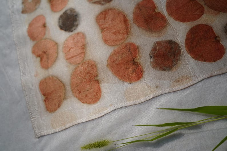 K&ouml;nnte beinhalten: Ein rechteckiges, cremewei&szlig;es Textil mit einem sich wiederholenden Muster aus gepressten, herzf&ouml;rmigen Bl&auml;ttern in Terrakotta-, Pfirsich- und Dunkelbraunt&ouml;nen. Der Stoff hat eine sichtbare Webstruktur und einen gen&auml;hten Saum am Rand.