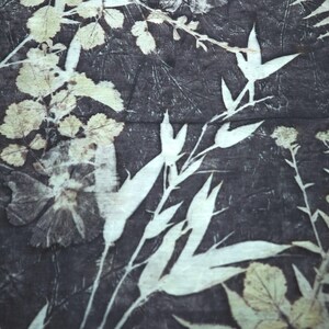 May include: A textile fabric featuring a dark charcoal gray background with a botanical print. The pattern consists of light cream-colored silhouettes of various leaves, stems, and flowers arranged in an overlapping, natural composition.