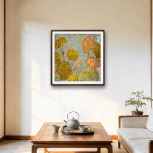 May include: A square framed wall art piece featuring a textured botanical illustration of golden-yellow and soft peach-colored lotus leaves and flowers against a light gray background, displayed in a dark brown wooden frame on a plain wall.