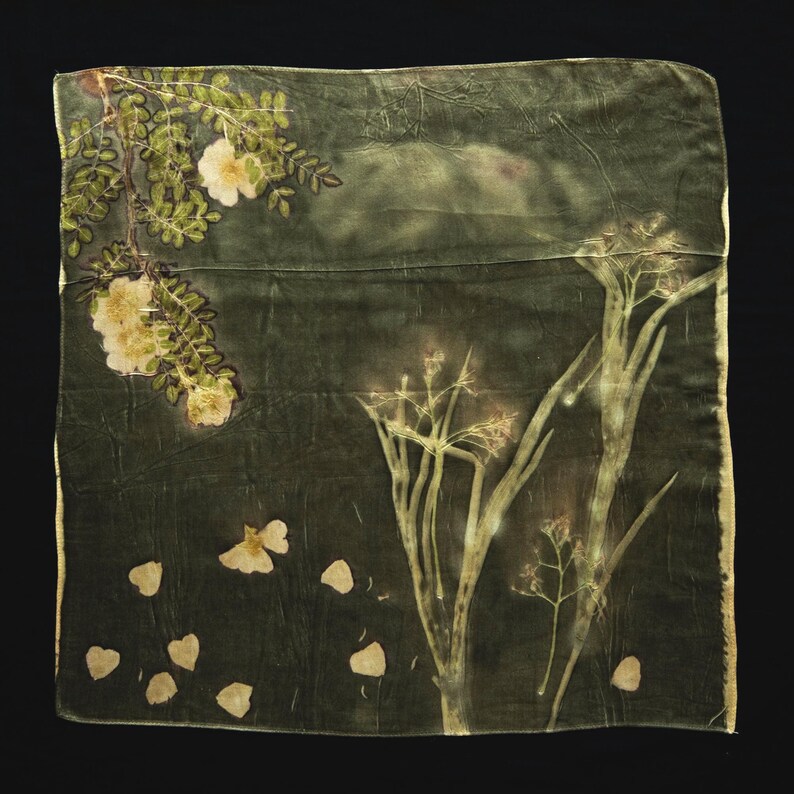 May include: A square textile piece in a deep forest green hue featuring botanical prints. The fabric displays a branch with pale yellow flowers in the upper left, scattered petals in the lower left, and tall, slender plant stalks on the right side.