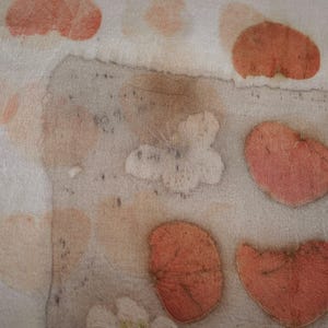 May include: A light-colored textile featuring a botanical print with repeating heart-shaped leaf patterns in shades of muted orange and soft pink. The fabric displays a textured, organic appearance with varying levels of color saturation across the surface.