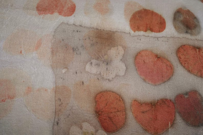 May include: A light-colored textile featuring a botanical print with repeating heart-shaped leaf patterns in shades of muted orange and soft pink. The fabric displays a textured, organic appearance with varying levels of color saturation across the surface.