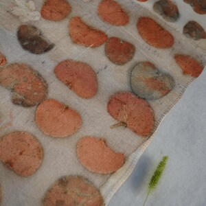 K&ouml;nnte beinhalten: Ein halbtransparenter, cremewei&szlig;er Stoffschal mit einem sich wiederholenden Muster aus botanischen Blattabdr&uuml;cken in Terrakotta-, Rost- und ged&auml;mpften Graut&ouml;nen. Das Textil weist eine nat&uuml;rliche Struktur mit sichtbaren Blattadern auf.