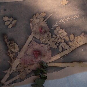 May include: A rectangular textile piece featuring a botanical print with dark grey and beige tones. The fabric displays pressed floral and leaf patterns in muted shades of pink, green, and brown, creating a natural, organic composition.