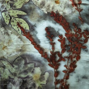 May include: A textile piece featuring a botanical print with dark gray and white marbled background tones. The fabric displays detailed imprints of light green leaves and vibrant rust-red sprigs, creating a natural, layered floral pattern across the surface.