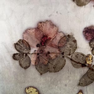 May include: A light-coloured fabric featuring botanical prints of a pink flower and dark brown leaves. The textile displays organic, pressed-plant patterns with visible veins and textures, creating a natural, earthy aesthetic across the surface.